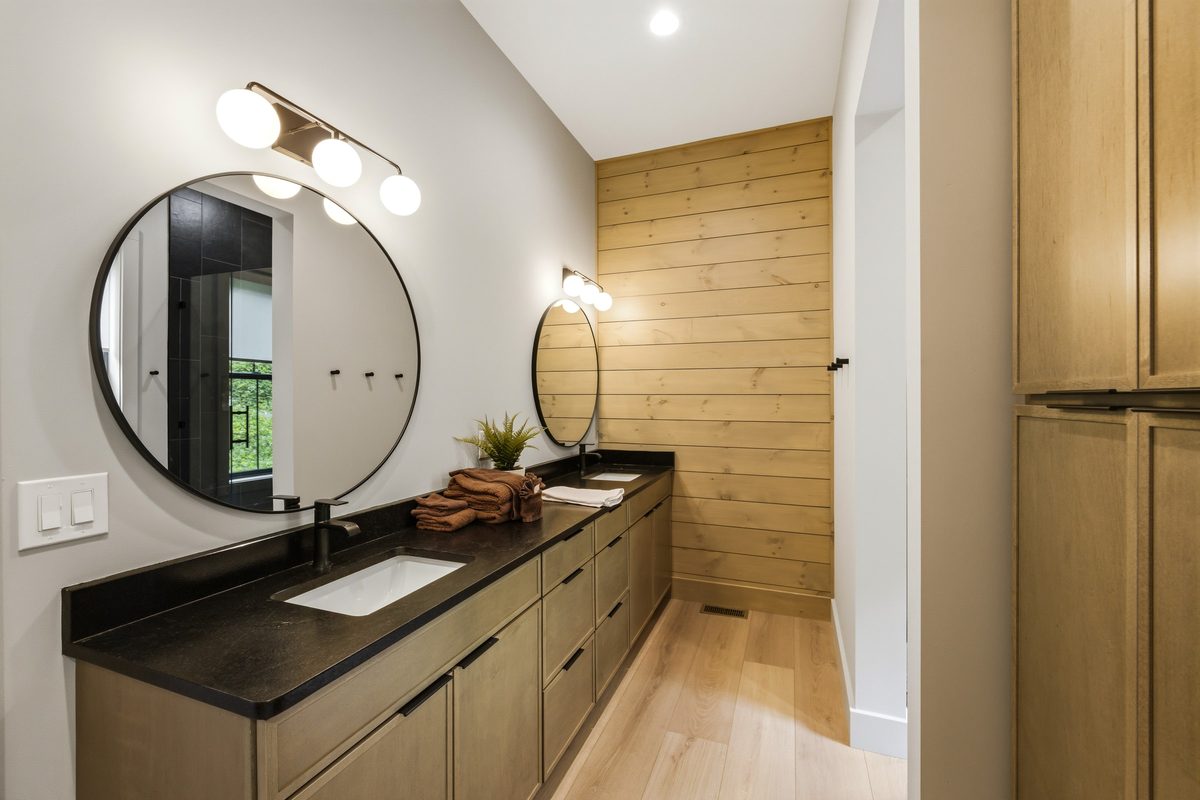 Bathroom with a long dark counter double vanity, round mirrors and a wood plank accent wall, Sevierville TN