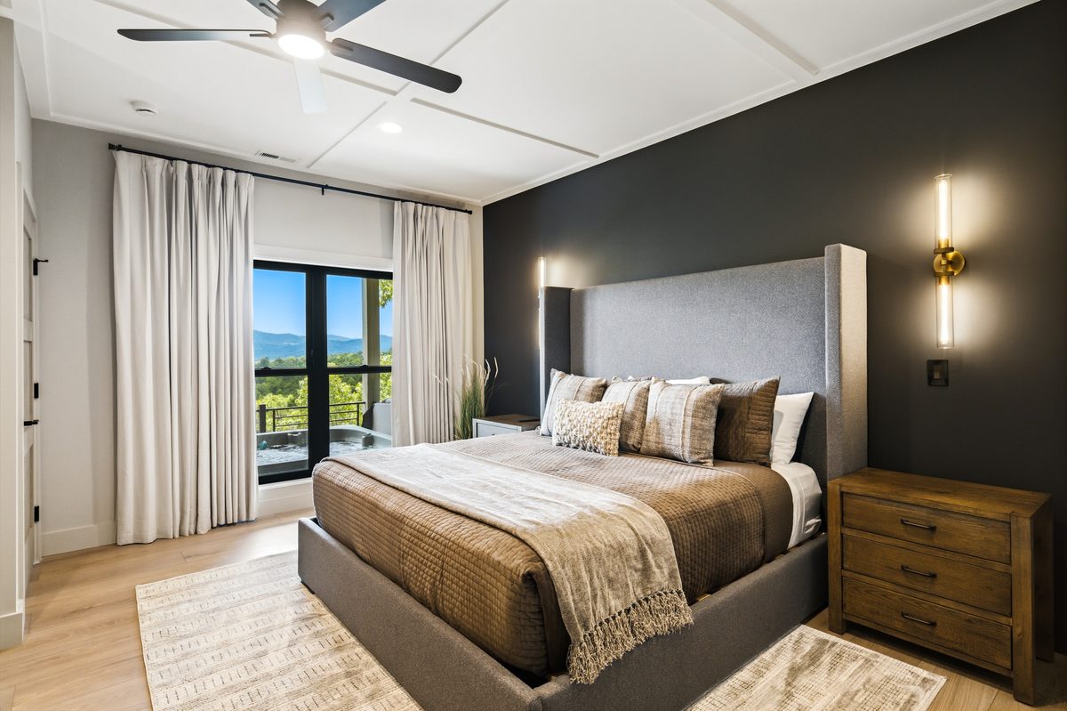 Bedroom with a dark accent wall, upholstered bed, brass sconces and glass doors to a mountain view, Sevierville TN