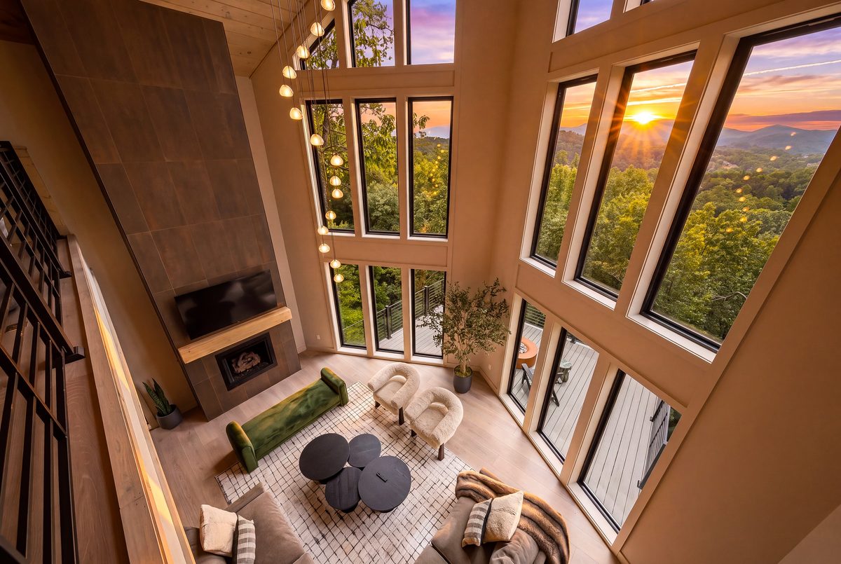 Two story great room at twilight with a sunset glowing through the window wall, a tall fireplace wall and a loft railing, Sevierville TN
