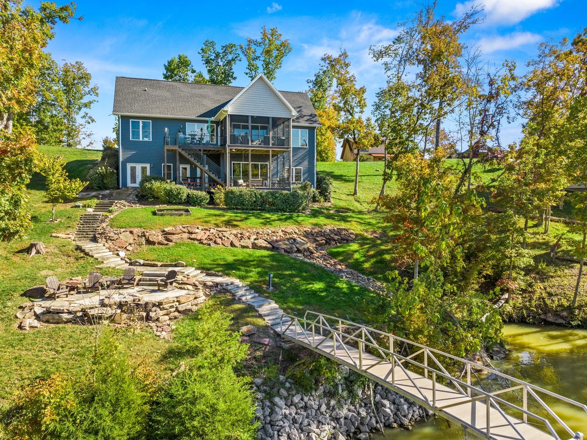 Aerial view of a blue lakefront home with stone terraces and a footbridge walkway down to the water, Ten Mile TN