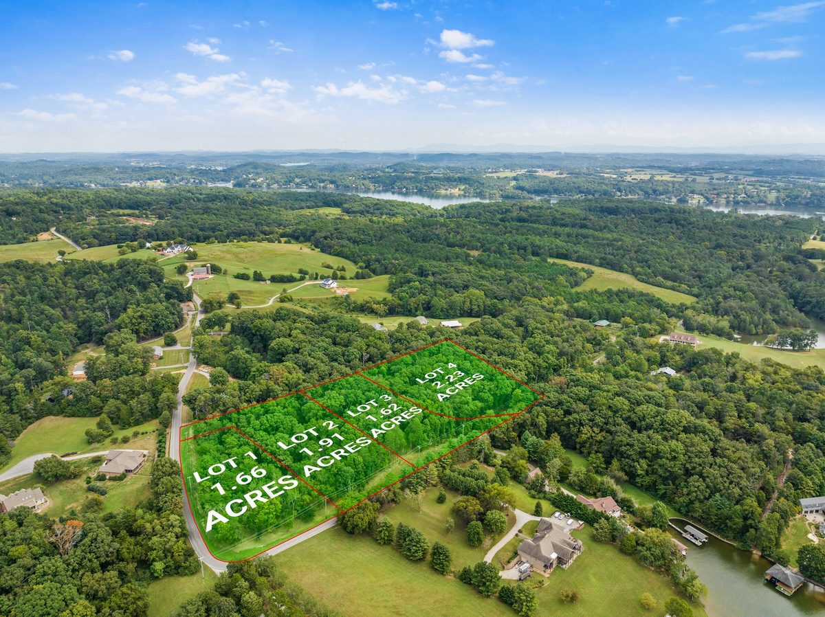 Aerial view of four adjoining wooded lots outlined with acreage labels beside a country road, with a lake beyond
